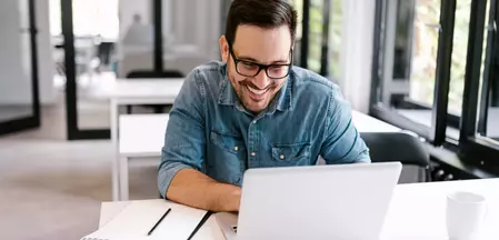 Das Foto zeigt einen Mann im Arbeitsmodus vor einem Laptop mit Stift und Block.